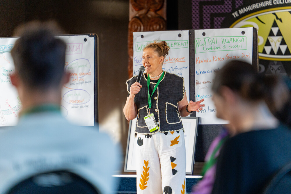 Centre for Social Impact Associate Miranda Cassidy-O’Connell speaks into a microphone while presenting to a group. Flip charts hang on the wall behind her.
